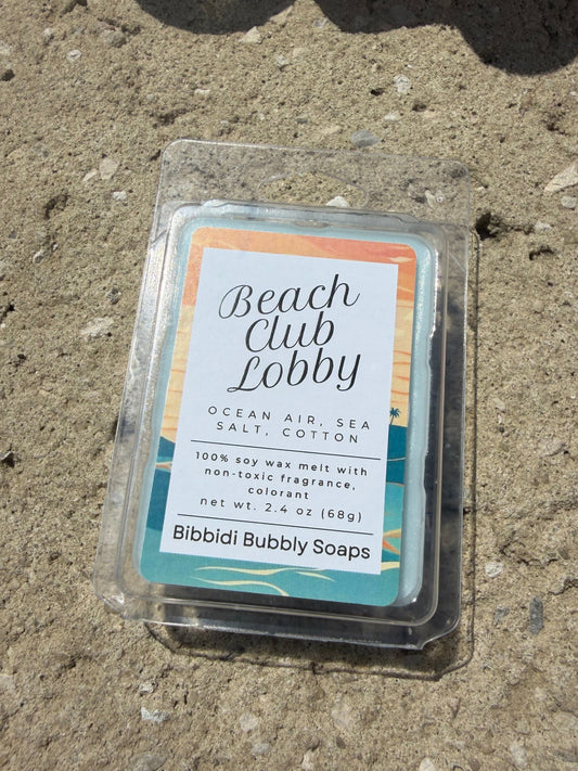 A wax melt package labeled Beach Club Lobby by Bibbidi Bubbly Soaps, placed on a textured concrete surface outdoors.
